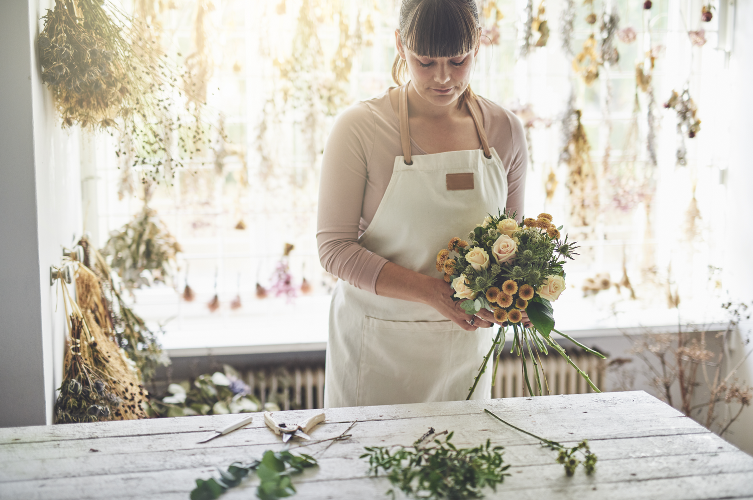 En kvinne i et forkle holder en bukett tørkede blomster.