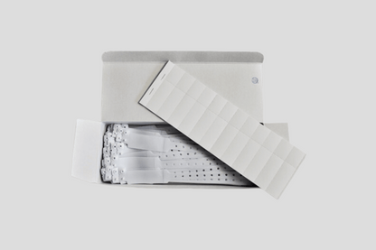 En hvit boks med en saks og en JM Band NO Pasientarmbånd plastik lomme På lager inni.
