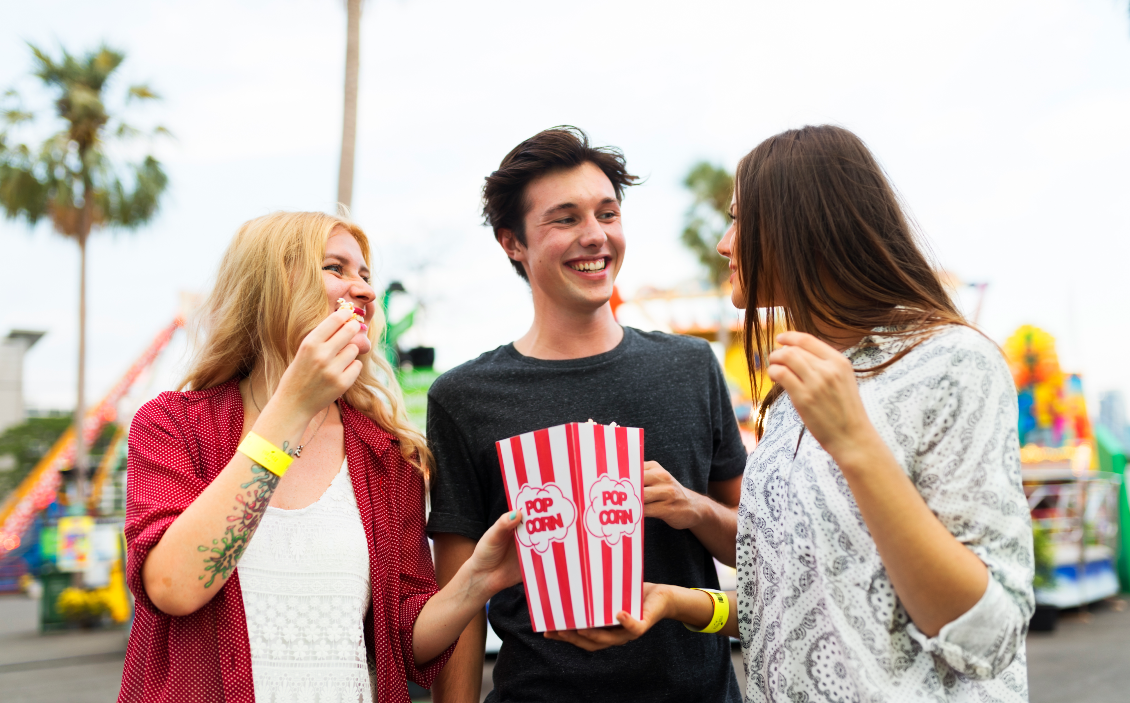 Tre unge mennesker spiser popcorn i en fornøyelsespark.