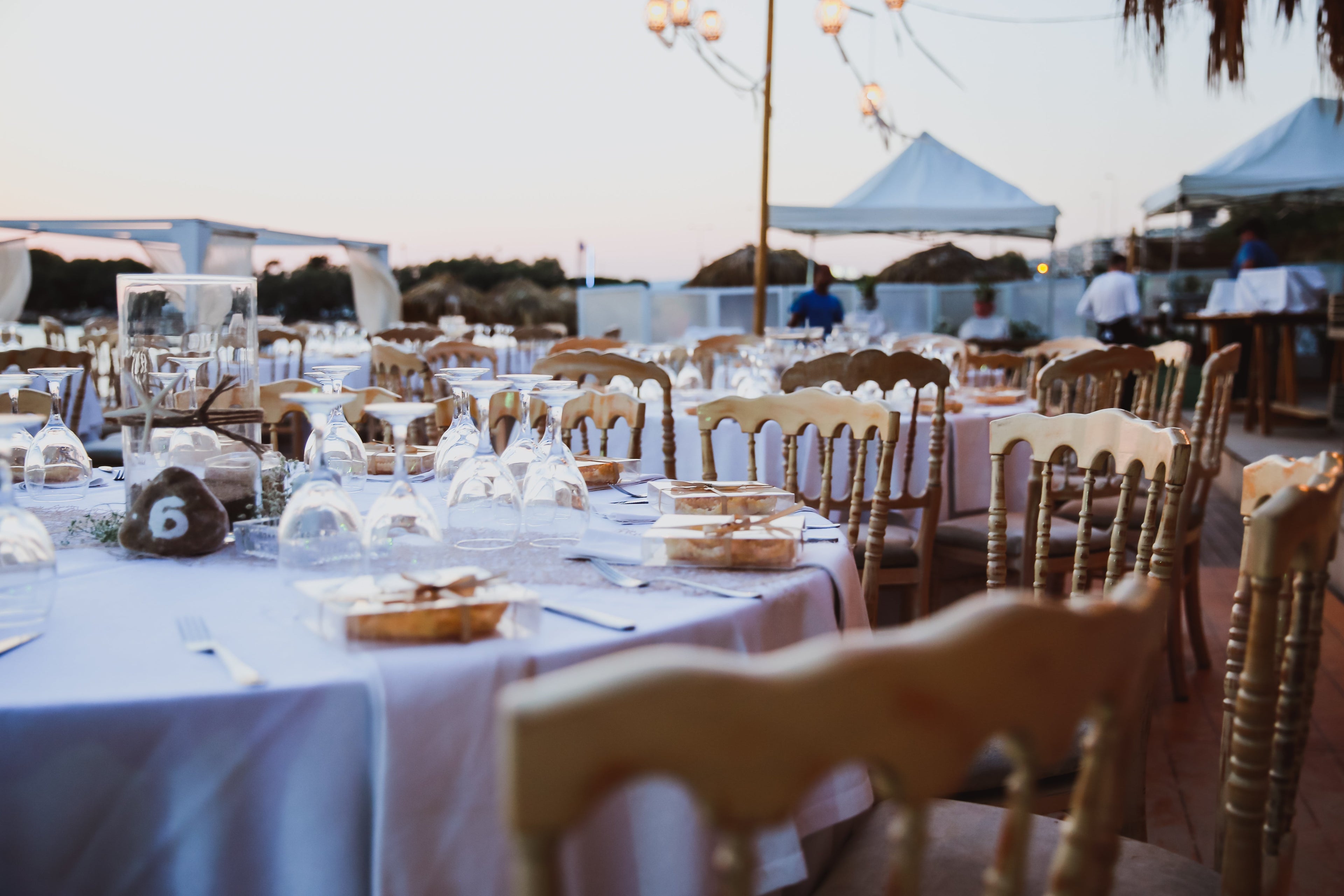 En bryllupsmottakelse satt opp på en strand med hvite bord og stoler.